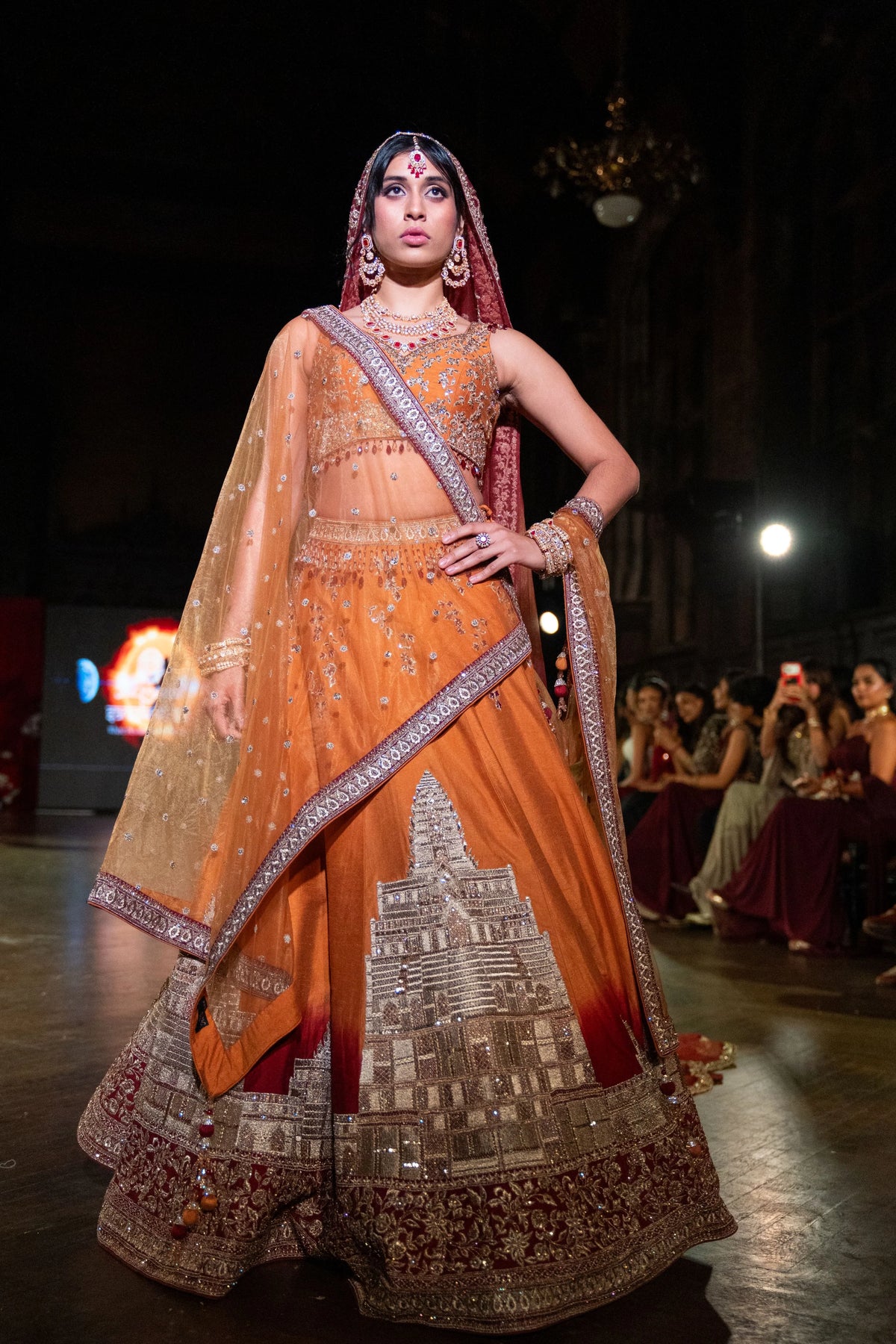 Angkor Wat sunset orange dupion lehenga with a gold temple-motif panel and red-bordered veil, model walking the runway
