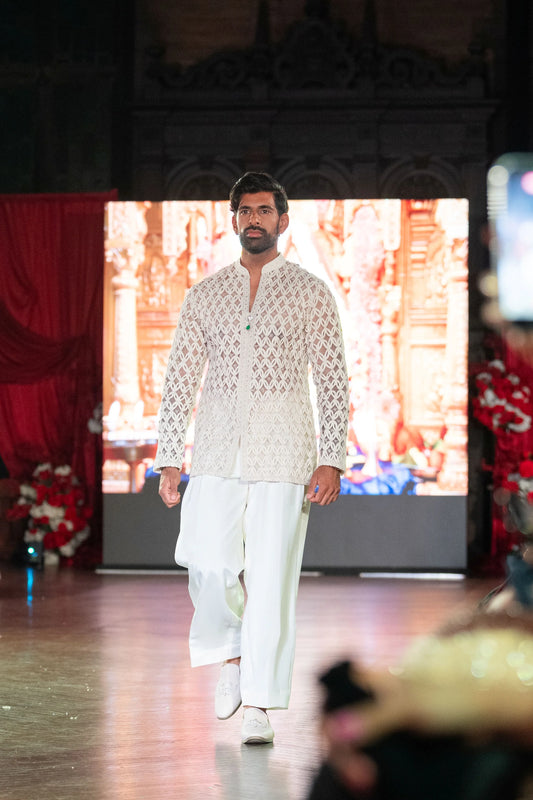 Model walking the runway in the Chitrakavya ivory lattice-embroidered jacket with ivory trousers in front of a temple screen