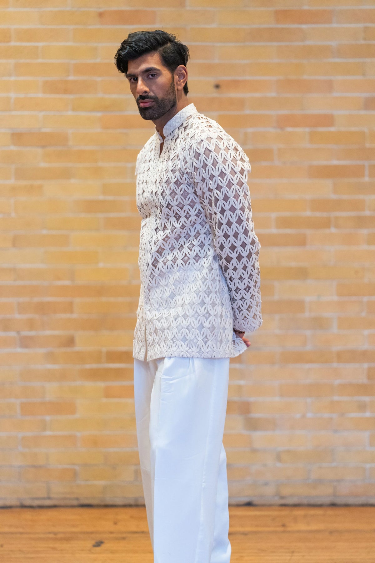 Side profile of the Chitrakavya ivory geometric-embroidered jacket with ivory trousers against a brick wall