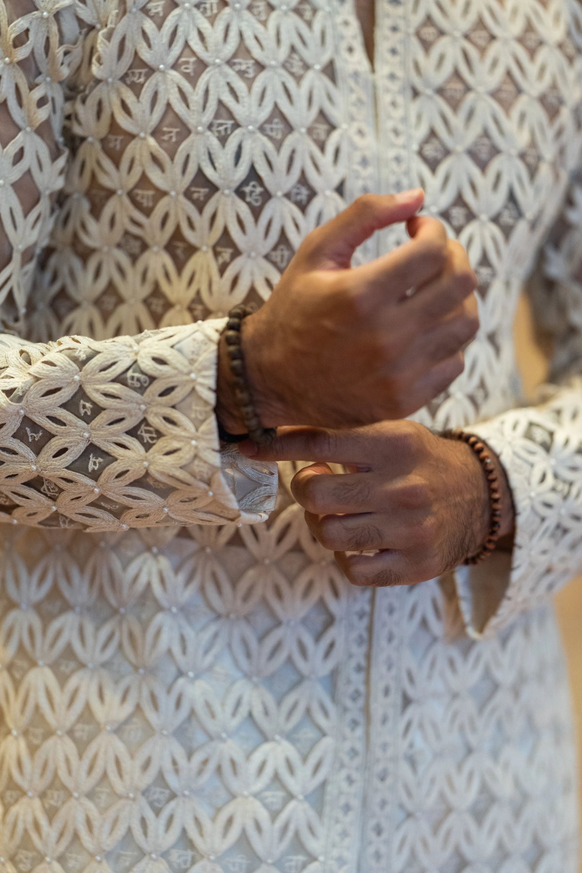 Close-up of the cutwork lattice sleeve on the Chitrakavya ivory jacket as the model adjusts his bracelets