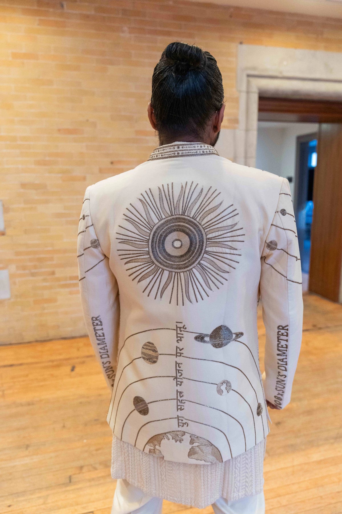 Back of the ivory Hanuman Chalisa jacket showing a large embroidered sun medallion and planetary orbit lines
