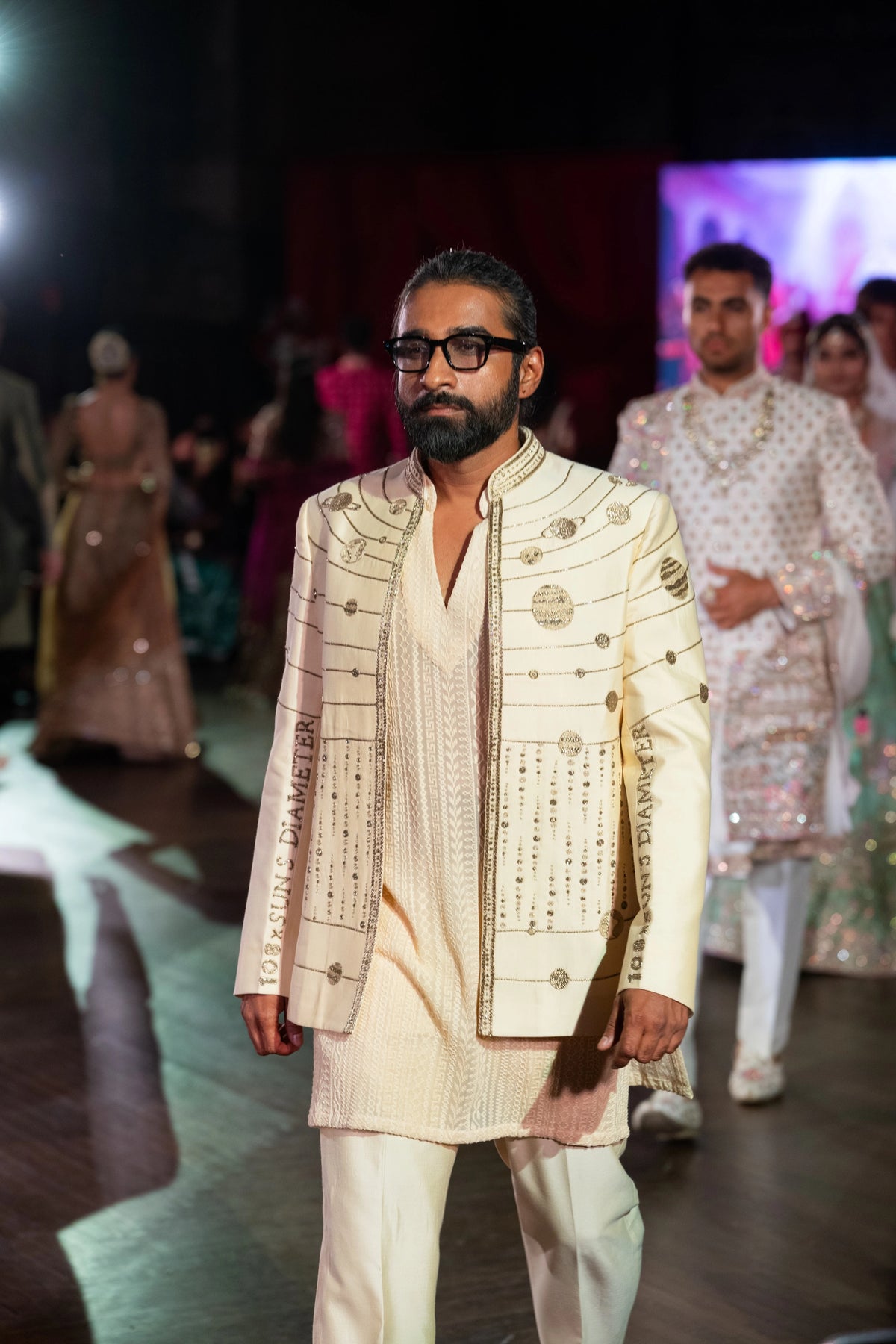 Model walking the runway in an ivory Hanuman Chalisa jacket with silver zardozi embroidery over an ivory kurta and pants