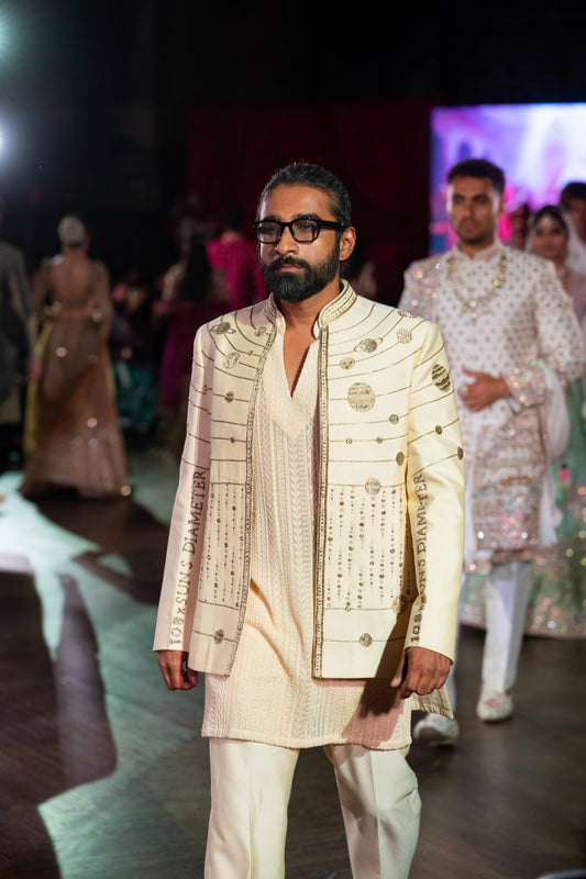 Model walking the runway in an ivory Hanuman Chalisa jacket with silver zardozi embroidery over an ivory kurta and pants