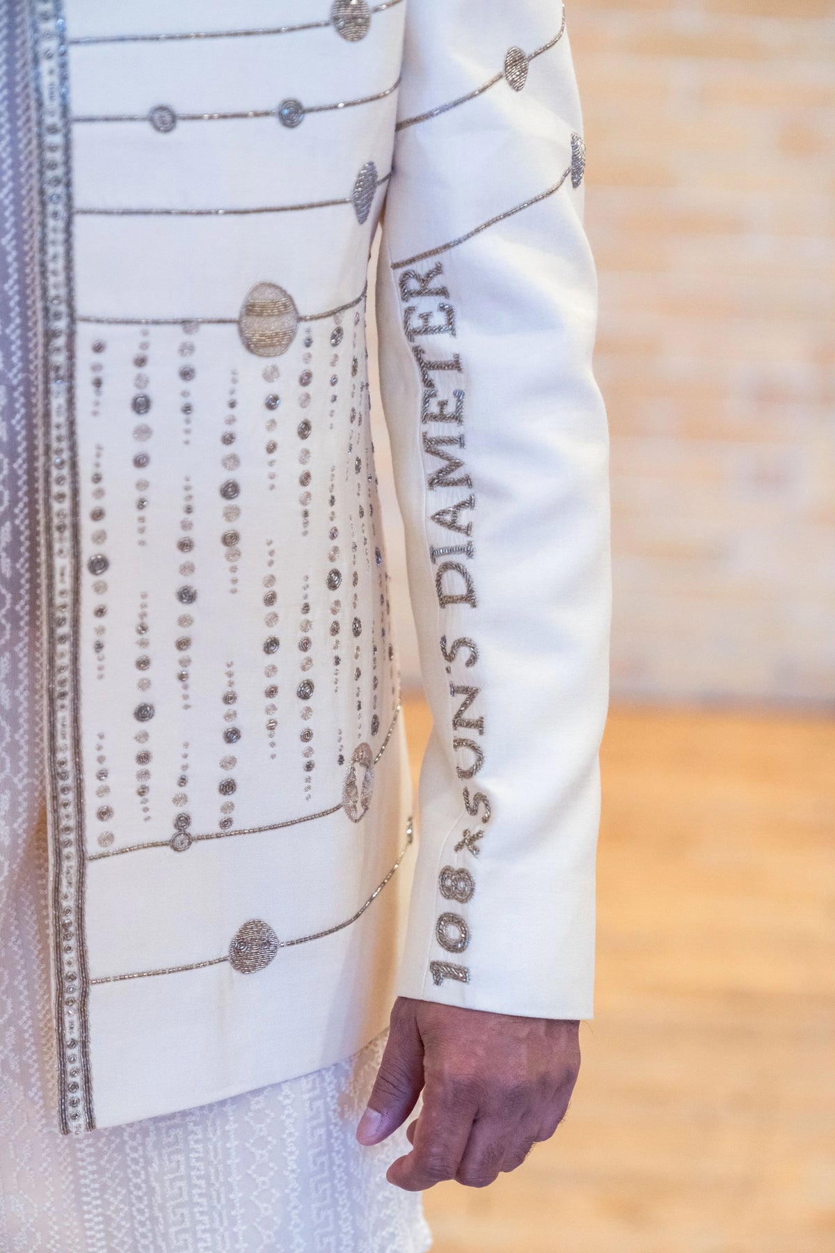 Sleeve of the ivory Hanuman Chalisa jacket with embroidered 108 Sun's Diameter lettering and beaded vertical lines