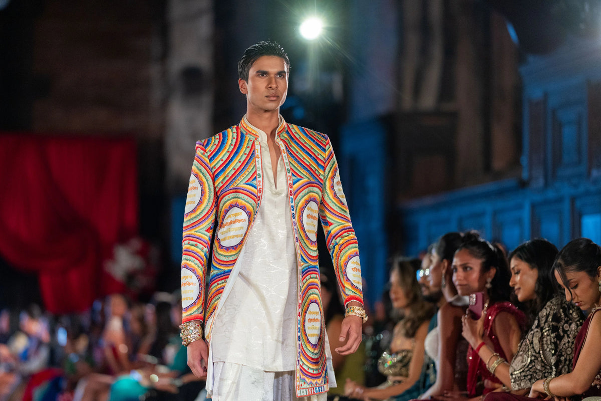 Wide runway view of the Katapayadi rainbow-ring jacket and white dhoti pants with seated audience