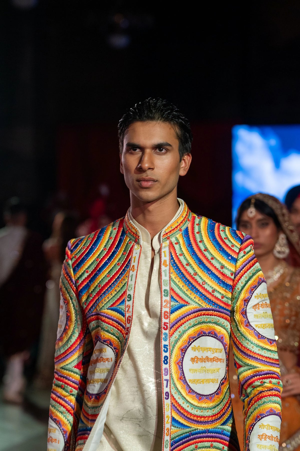 Close portrait of the Katapayadi jacket with bands of orange, blue and yellow circles over an ivory kurta