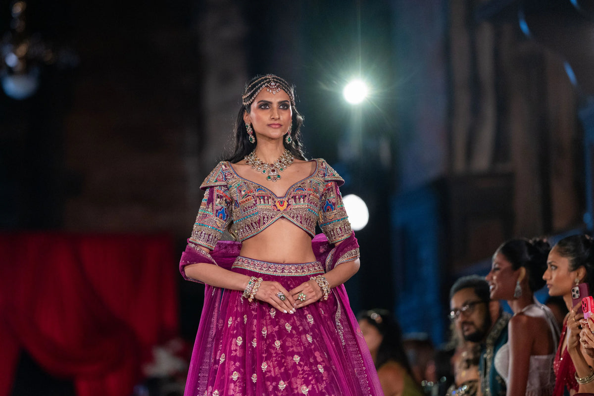 Half-length runway view of the Meenakshi Temple magenta lehenga and embroidered blouse with seated audience behind