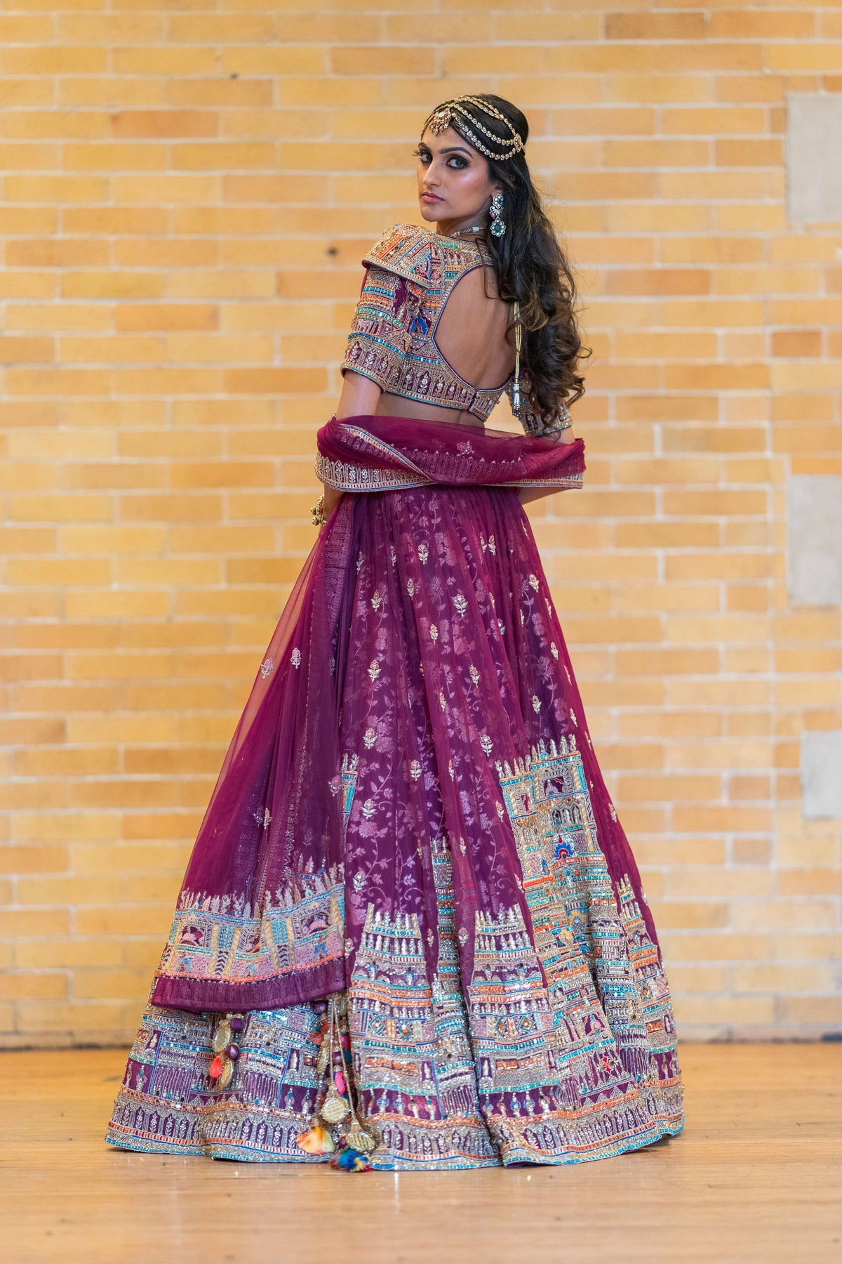 Back view of the Meenakshi Temple magenta lehenga with an open-back embroidered blouse against a brick wall