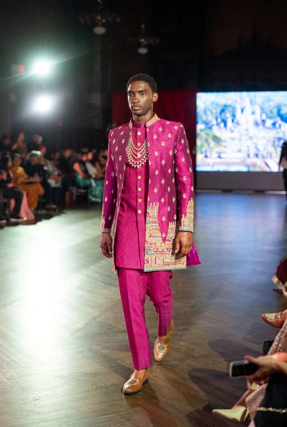 Close front view of the magenta sherwani with pearl necklace and embroidered panels, model walking the runway