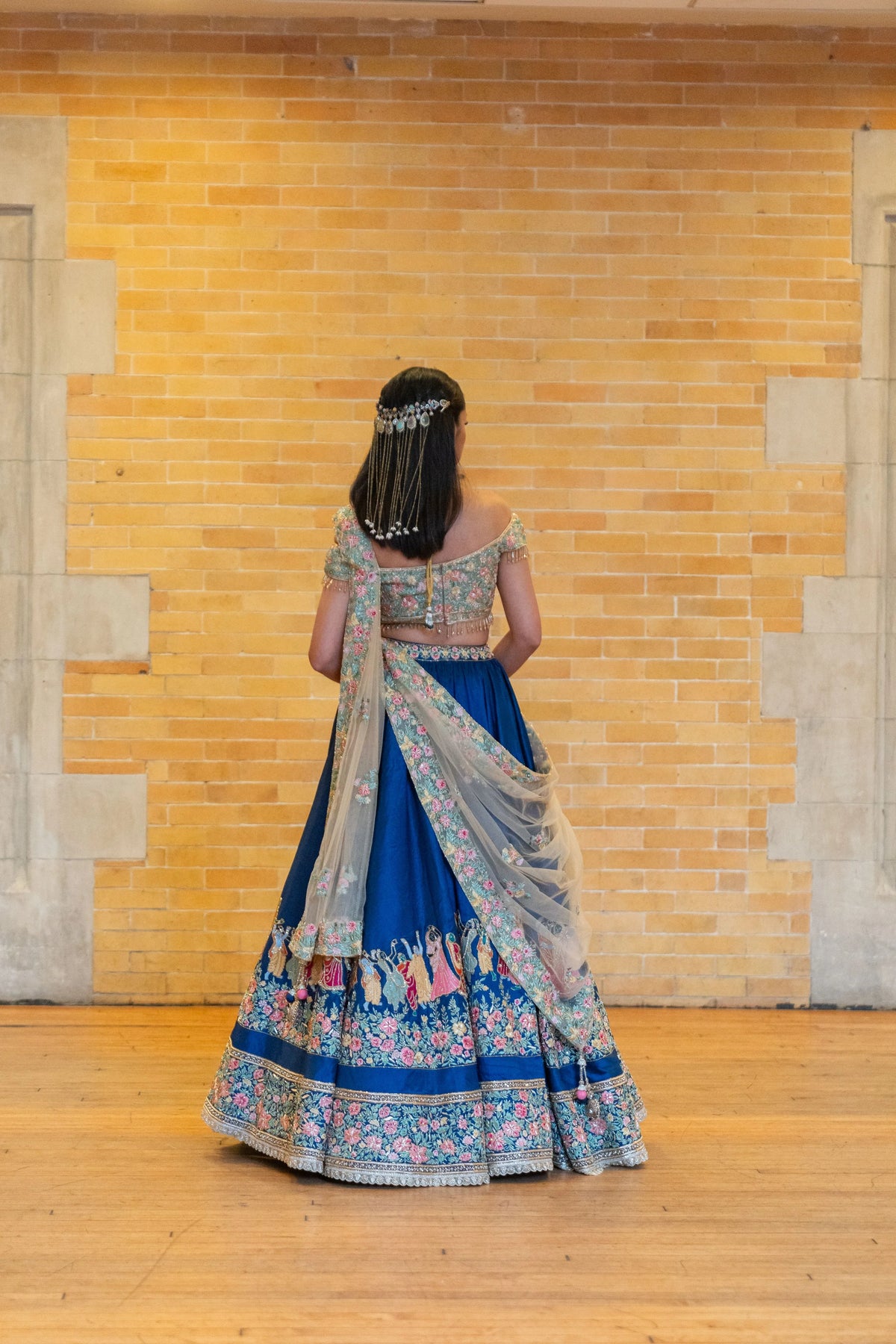 Back view of the Raas Leela blue lehenga with a floral border and gold net dupatta against a brick wall