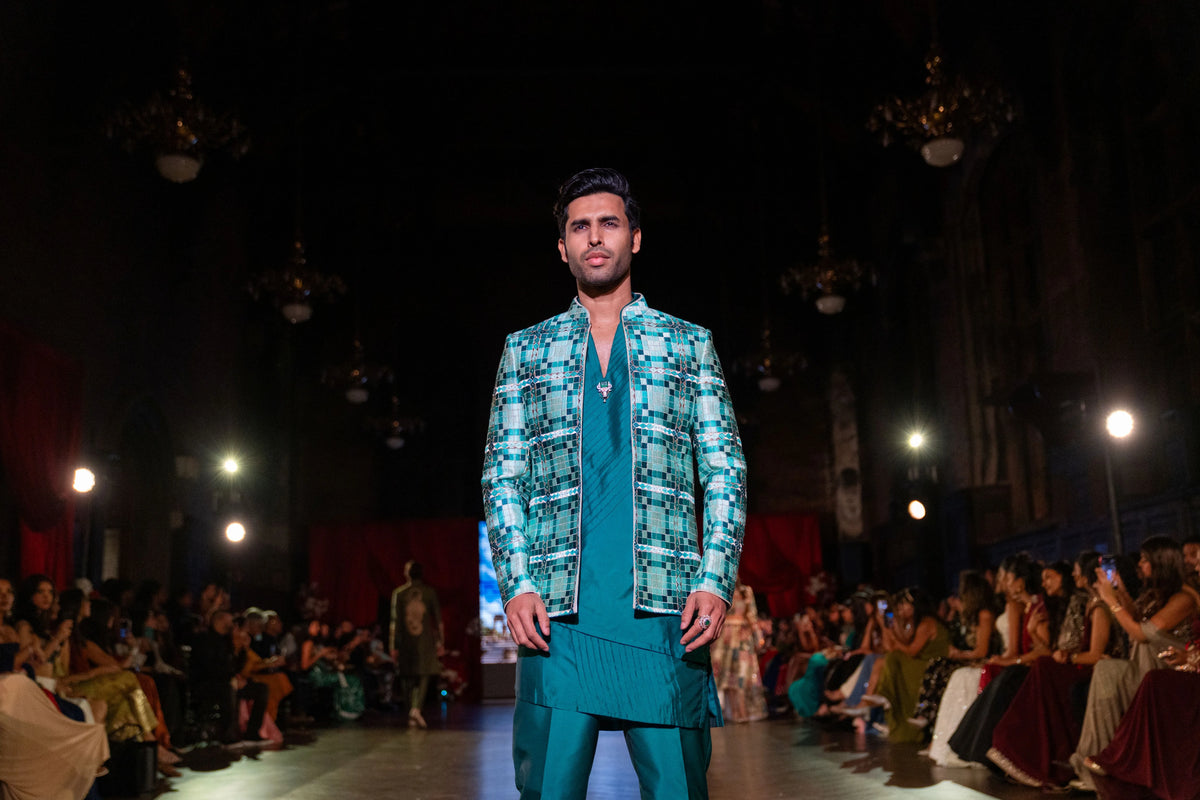 Wide runway view of the Sarvatobhadra green jacket and teal ensemble, hands at his sides