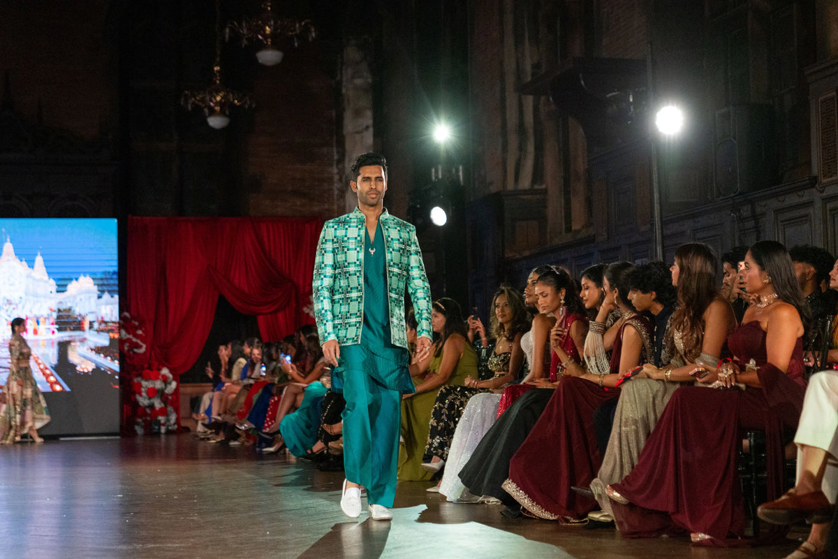 Side-angled runway view of the Sarvatobhadra green jacket and teal pants with a temple image on screen