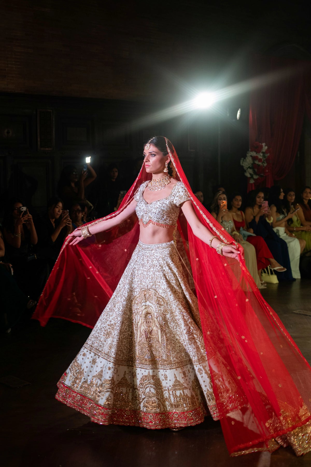 Siddhivinayak lehenga with the red dupatta spread wide as the model holds her arms out on the runway
