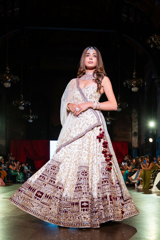 Venkateshwara ivory lehenga with a maroon temple-pattern hem, model standing at three-quarter angle