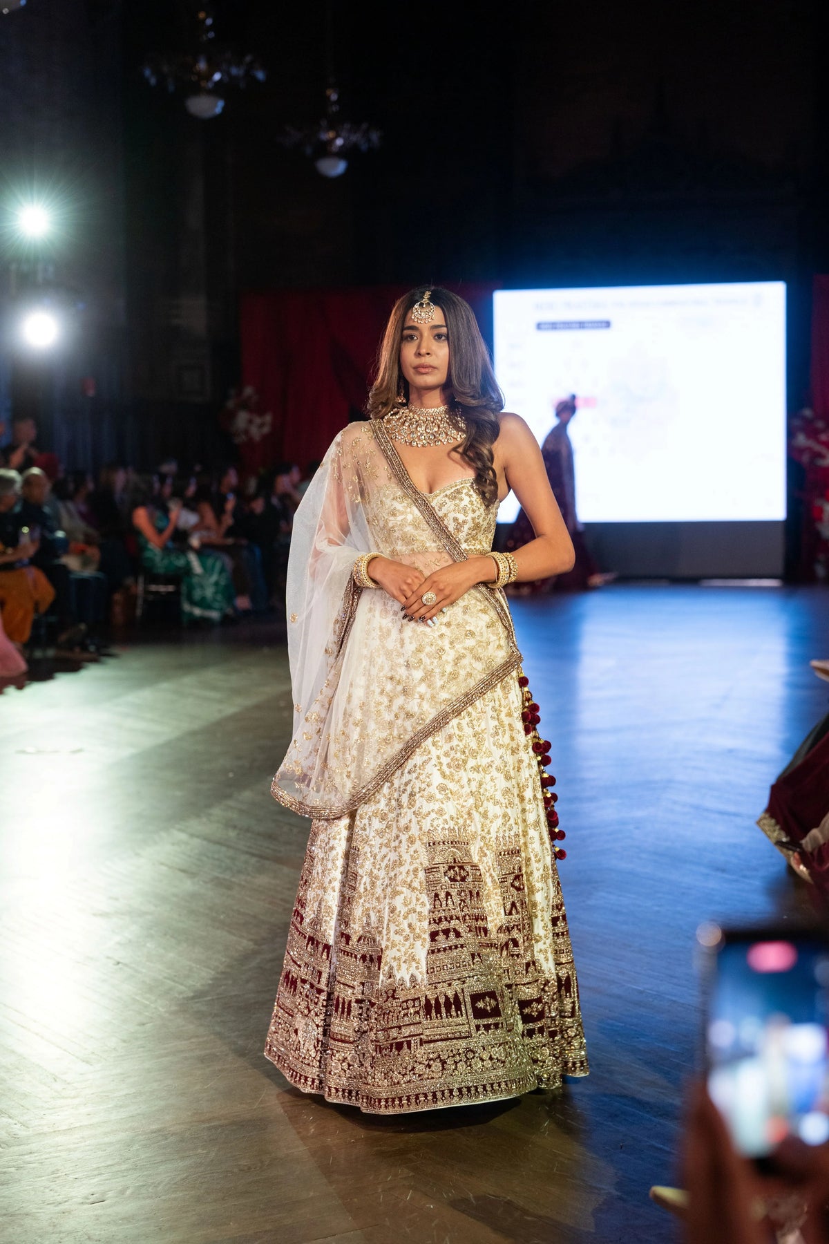 Full-length front view of the Venkateshwara ivory and maroon lehenga on a dark stage
