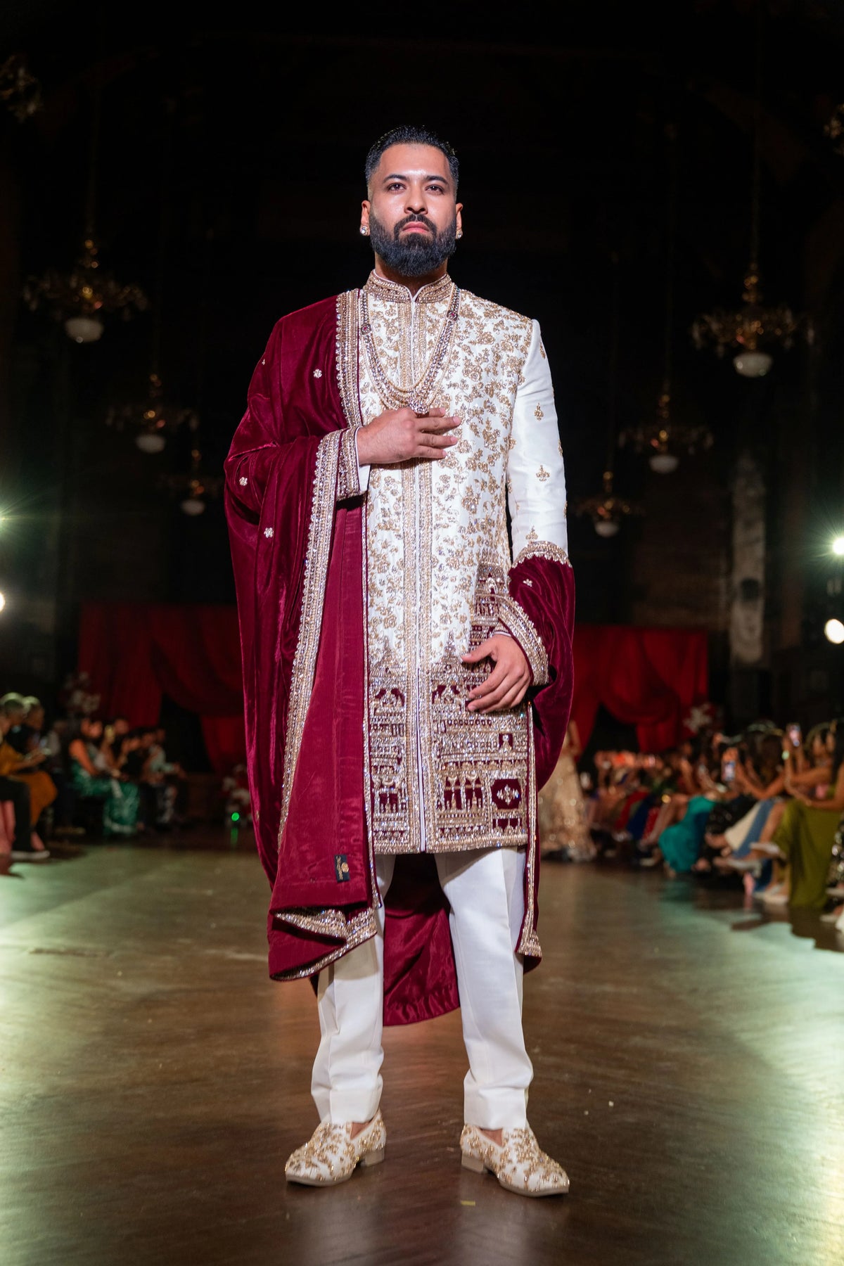Venkateshwara ivory and gold embroidered sherwani with a maroon velvet shawl, model with a hand on his chest