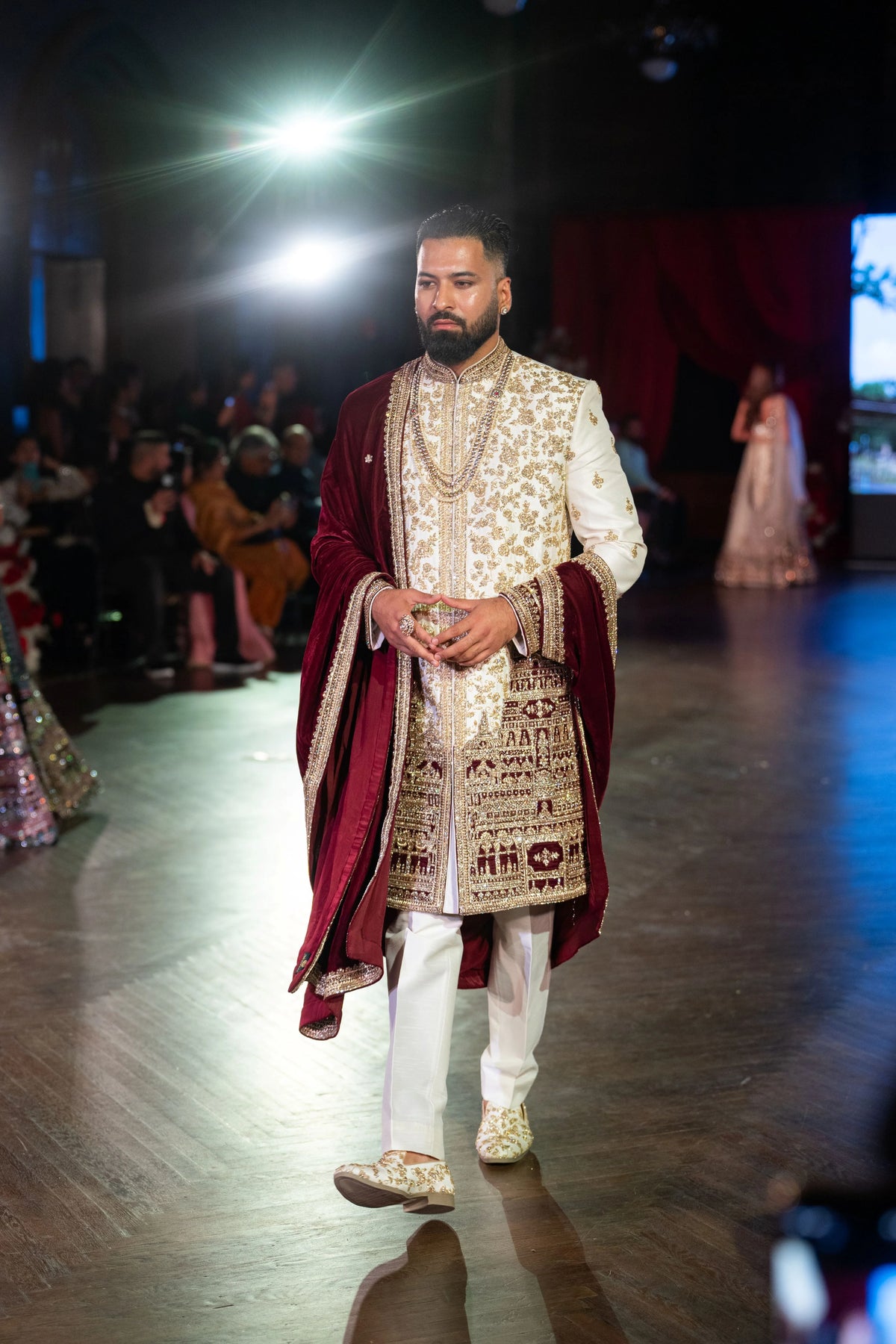 Venkateshwara ivory sherwani with a maroon velvet shawl and white trousers, model walking on the runway