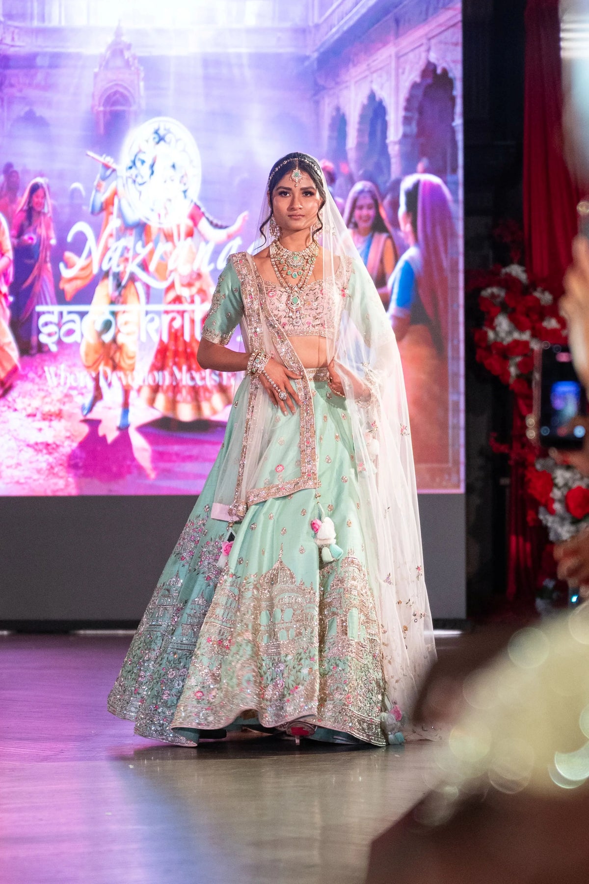Vrindavan mint green lehenga with a veil dupatta, model standing in front of the stage screen